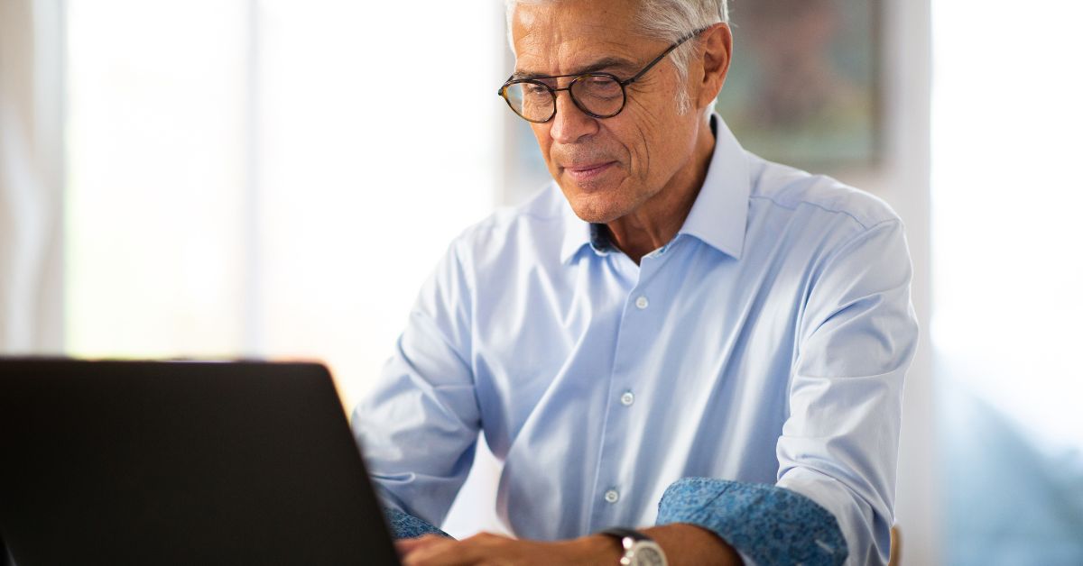 An older man using a laptop computer to see what is the cost of living in Dallas TX.