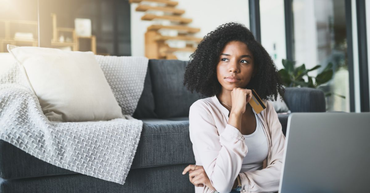 A young black woman sitting on the floor with a laptop researching construction costs in Austin.